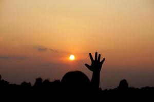 silhouet van menselijk hand- verheven naar maken een wens, zonsondergang achtergrond foto