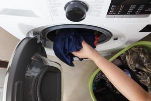 bovenaanzicht van de hand van een vrouw die vuile kleren in de wasmachine stopt. foto