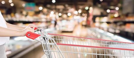 vrouw hand- houden leeg rood boodschappen doen kar met abstract vervagen supermarkt korting op te slaan gangpad interieur onscherp achtergrond met bokeh licht foto