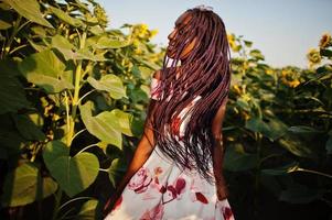 mooie jonge zwarte vrouw draagt zomerjurk pose in een zonnebloemveld. foto