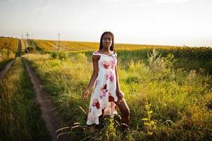 mooie jonge zwarte vrouw draagt zomerjurk pose in een zonnebloemveld. foto