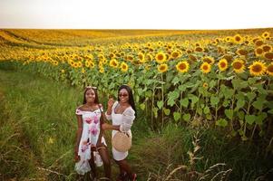 twee mooie jonge zwarte vrienden vrouw dragen zomerjurk poseren in een zonnebloemveld. foto