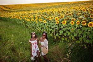 twee mooie jonge zwarte vrienden vrouw dragen zomerjurk poseren in een zonnebloemveld. foto