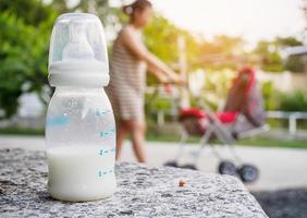 babymelkfles op stenen tafel over moeder met kinderwagenachtergrond foto