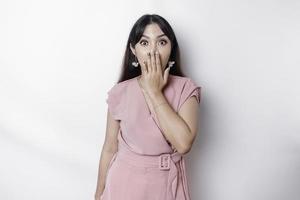 verrast jong Aziatisch vrouw aan het bedekken mond met handen en staren Bij camera terwijl staand tegen wit achtergrond foto