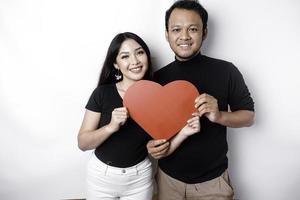 een jong Aziatisch paar glimlachen en Holding rood hartvormig papier, geïsoleerd door wit achtergrond foto