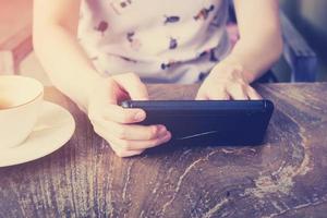 hand- vrouw gebruik makend van smartphone in koffie winkel en zacht licht met wijnoogst filter. foto