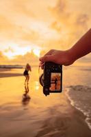 een camera met handen foto's een balinees vrouw aan het doen een gymnastiek- beweging Aan een zwart overhemd in de buurt de strand foto