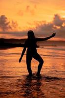 een balinees vrouw in de het formulier van een silhouet presteert ballet bewegingen heel behendig en flexibel Aan de strand met de golven crashen foto