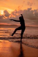 een Indonesisch vrouw in silhouet aan het doen een mooi dans Aan de strand met de crashen golven in de middag foto