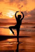 een ballerina met een silhouet vorm presteert ballet bewegingen heel flexibel Aan de strand met de golven crashen foto