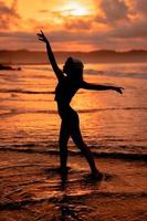 silhouet van een heel slank ballerina aan het doen ballet praktijk alleen Aan de kust met golven crashen Bij haar foto