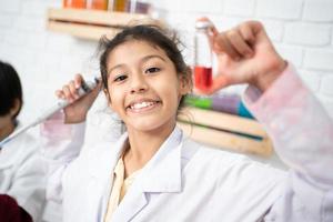 lief weinig meisje wetenschapper genieten en prikkelen naar onderzoeken de kleur chemisch in laboratorium door gebruik makend van druppelaar met dag licht. opgewonden kind vieren over- geslaagd wetenschap experiment resultaat of chemisch foto