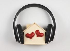 vlak leggen van houten model- huis met twee rood schitteren harten gedekt met hoofdtelefoons geïsoleerd Aan wit achtergrond. muziek- of podcast, huis van liefde, valentijnskaarten. foto