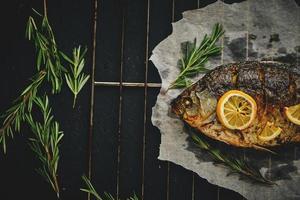 vis gebakken in oven met citroen en rozemarijn Aan perkament papier, gelegd uit Aan rooster donker achtergrond. foto