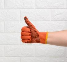 vrouw hand- in een oranje werk beschermend handschoen shows de gebaar Leuk vinden Aan een wit steen achtergrond foto