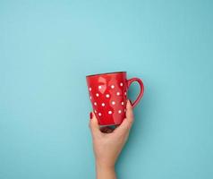 vrouw hand- Holding een rood keramisch mok Aan een blauw achtergrond, breken tijd foto