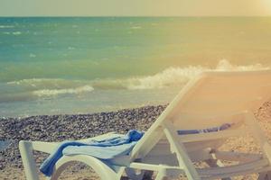 zonnebank Aan een zanderig zee strand met zonnestralen. kilte en ontspanning Aan vakantie. kopiëren ruimte Aan water achtergrond foto