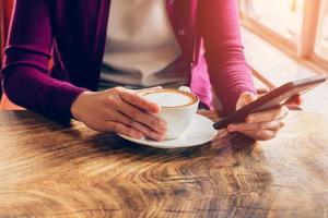 vrouw gebruik makend van mobiel telefoon in cafe. vrouw Holding kop en koffie. foto