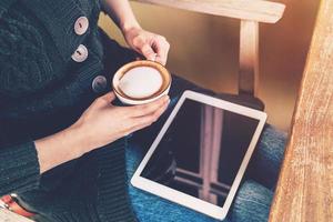 dichtbij omhoog Aziatisch vrouw Holding koffie en tablet in koffie winkel met wijnoogst filter. foto