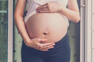 dichtbij omhoog hand- zwanger vrouw Holding haar buik foto