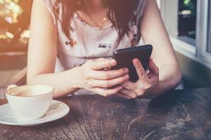 dichtbij omhoog van hand- vrouw gebruik makend van telefoon in koffie winkel met wijnoogst afgezwakt. foto