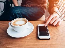 dichtbij omhoog hand- Mens gebruik makend van telefoon in koffie winkel met wijnoogst filter. foto