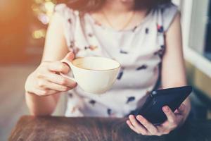 dichtbij omhoog van hand- vrouw gebruik makend van telefoon in koffie winkel met diepte van veld, wijnoogst afgezwakt. foto