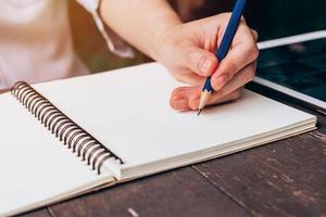 Aziatisch vrouw hand- schrijven potlood Aan notitieboekje in koffie winkel met wijnoogst afgezwakt foto