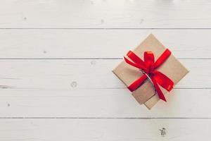 bruin geschenk doos met label Aan houten achtergrond. wijnoogst geschenk doos Aan houten achtergrond. geschenk doos met rood lint Aan hout achtergrond met ruimte. foto