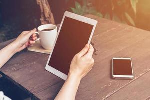 dichtbij omhoog hand- Holding en gebruik makend van tablet in koffie winkel met wijnoogst afgezwakt. foto