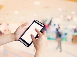 hand- vrouw Holding en gebruik makend van telefoon met wazig achtergrond in boodschappen doen winkelcentrum. foto