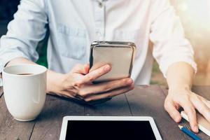 vrouw hand- Holding telefoon en gebruik makend van telefoon Aan tafel in tuin Bij koffie winkel met wijnoogst afgezwakt. foto