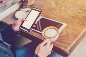 hand- vrouw gebruik makend van smartphone in koffie winkel en zacht licht met wijnoogst filter. foto