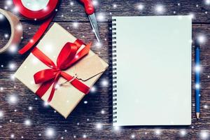 bruin geschenk doos en notitieboekje, potlood met sneeuw wit Aan hout bord achtergrond met ruimte. foto