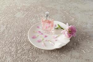 een chique fles van vrouwen toilet water of parfum staat Aan een wit abstract bord met bloemblaadjes en een lila bloem. grijs achtergrond. een kopiëren ruimte. foto