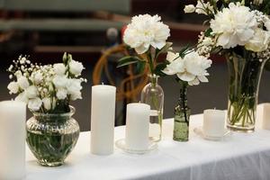 tafel dekken bij huwelijksreceptie. bloemencomposities met prachtige bloemen en groen, kaarsen op versierde tafel. gezelligheid en stijl. modern evenementontwerp. selectieve aandacht. foto