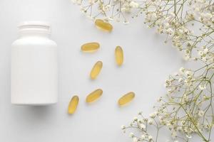 olie gele gelatine capsules met witte fles op witte achtergrond met bloemen, vitamines en antioxidant concept omega 3, lever kabeljauw of teunisbloemolie voor de gezondheidszorg. minimalisme. ruimte kopiëren. foto