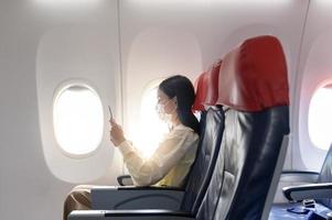 een jonge vrouw met een gezichtsmasker reist met het vliegtuig, nieuw normaal reizen na covid-19 pandemisch concept foto
