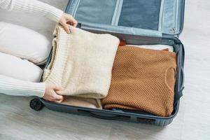 vrouw hand- inpakken haar winter kleren in bagage. tijd naar reis, reis, kom tot rust, voorjaar of herfst of winter seizoen en vakantie concepten foto