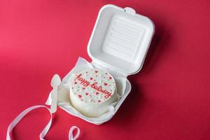 een klein bento taart met belettering en harten in een doos met een houten lepel. rood achtergrond foto