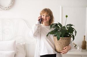 een geslaagd emotioneel Europese meisje in een wit overhemd maakt een bedrijf telefoongesprek. binnen- planten foto