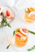 verfrissend grapefruit cocktail met rozemarijn in bril en fruit Aan een bord Aan de tafel. eigengemaakt drankje. verticaal visie foto