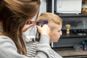 een schooljongen is zittend in een kapperszaak, aan het doen zijn haar- met een tondeuse foto