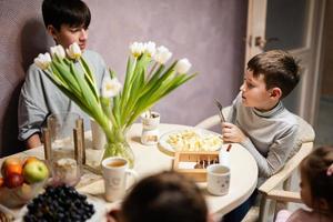 kinderen eten fruit en toetjes, drinken thee Bij huis in de avond keuken. chocola Aan een stok voor smeltend. foto