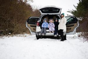 moeder met drie kinderen zitten Aan auto suv met Open romp staan in winter Woud. foto