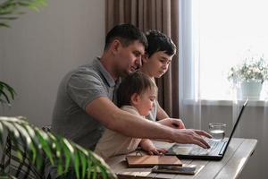 een Mens werken Bij huis met een laptop en looks na de kinderen. vader freelancer proberen naar werk Bij huis met kinderen. huis kantoor en ouderschap Bij de dezelfde tijd foto