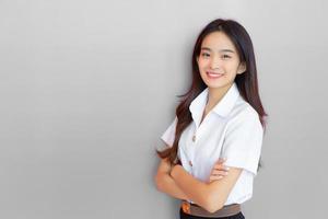 portret van volwassen Thais leerling. mooi Aziatisch jong vrouw leerling in uniform is glimlachen en op zoek Bij camera met haar armen gekruiste vol vertrouwen Aan grijs achtergrond in de Universiteit foto