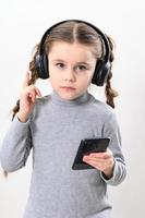 een meisje met hoofdtelefoons en een telefoon Aan een wit achtergrond, een meisje met vlechten luistert naar muziek- in koptelefoon, foto met kopiëren ruimte.