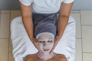 vrouw met haar gezicht gedekt met gaas voor huid behandeling ontvangen massage door schoonheidsspecialist foto